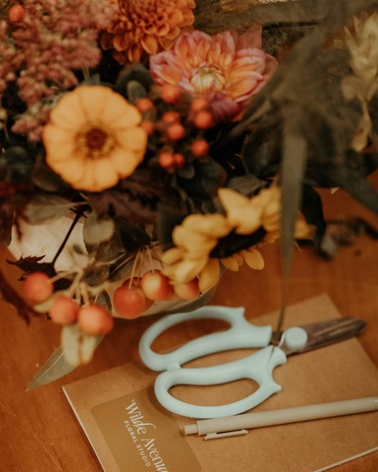 Floral arrangement with scissors and a notebook on a wooden surface