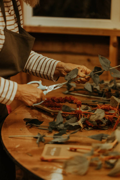 Person arranging dried flowers on a wooden table with scissors.